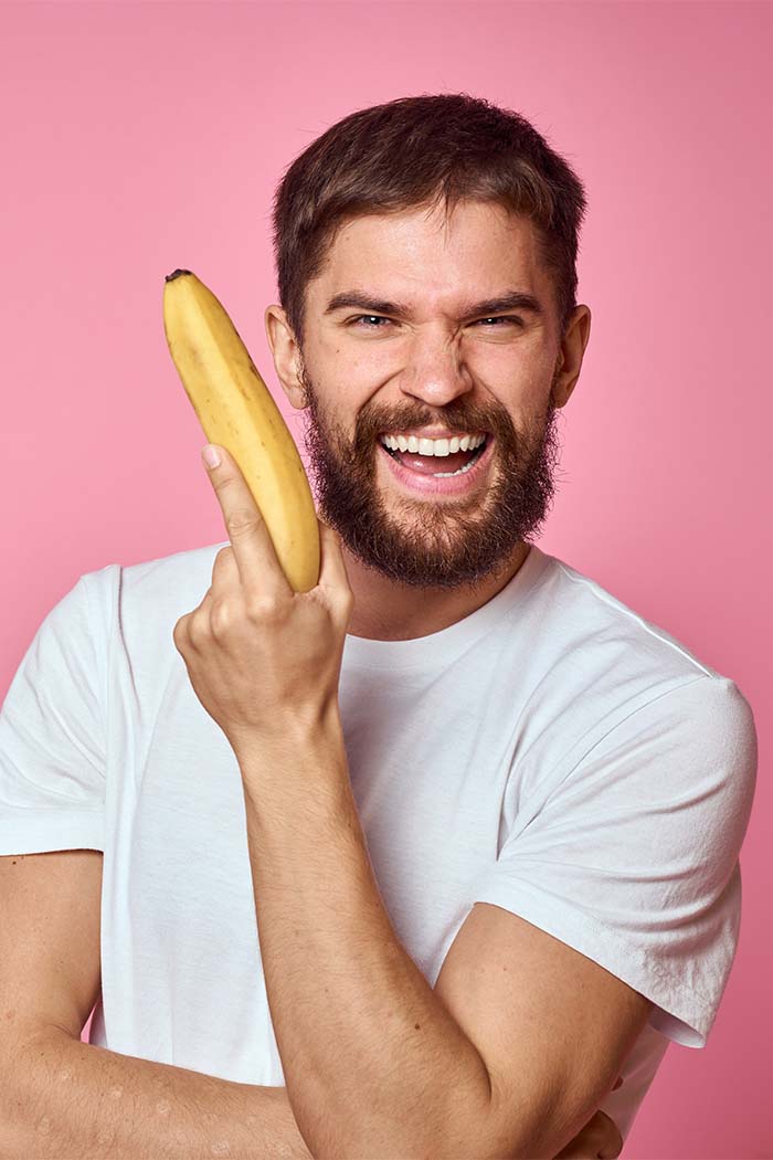 Man smiling while holding a banana in front of a pink background